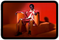 iPad mini displayed, front view, screen showing a vivid screen with a person in an orange suit, sitting on an orange chair, placed in an orange room