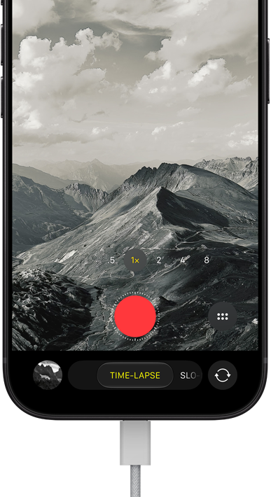 iPhone 18 Pro, front exterior, displaying a mountainous landscape, with the camera mode overlay in Time-Lapse mode, with power cable attached to charging port