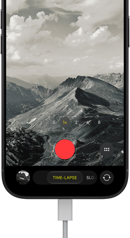 iPhone 18 Pro, front exterior, displaying a mountainous landscape, with the camera mode overlay in Time-Lapse mode, with power cable attached to charging port